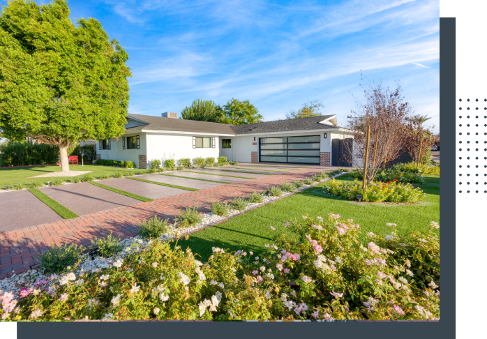 A large white house with a driveway and flowers in the yard.