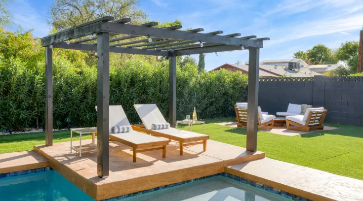 A wooden pergola with two lounge chairs next to the pool.