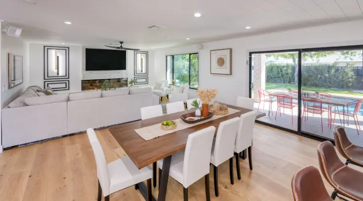 A dining room table with white chairs and a television.