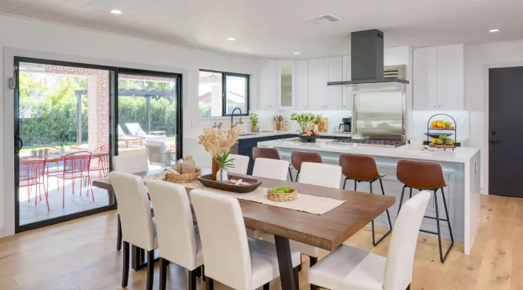 A dining room table with white chairs and a kitchen in the background.