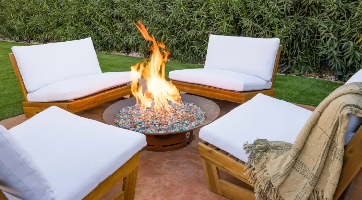 A fire pit with white chairs and pillows around it.