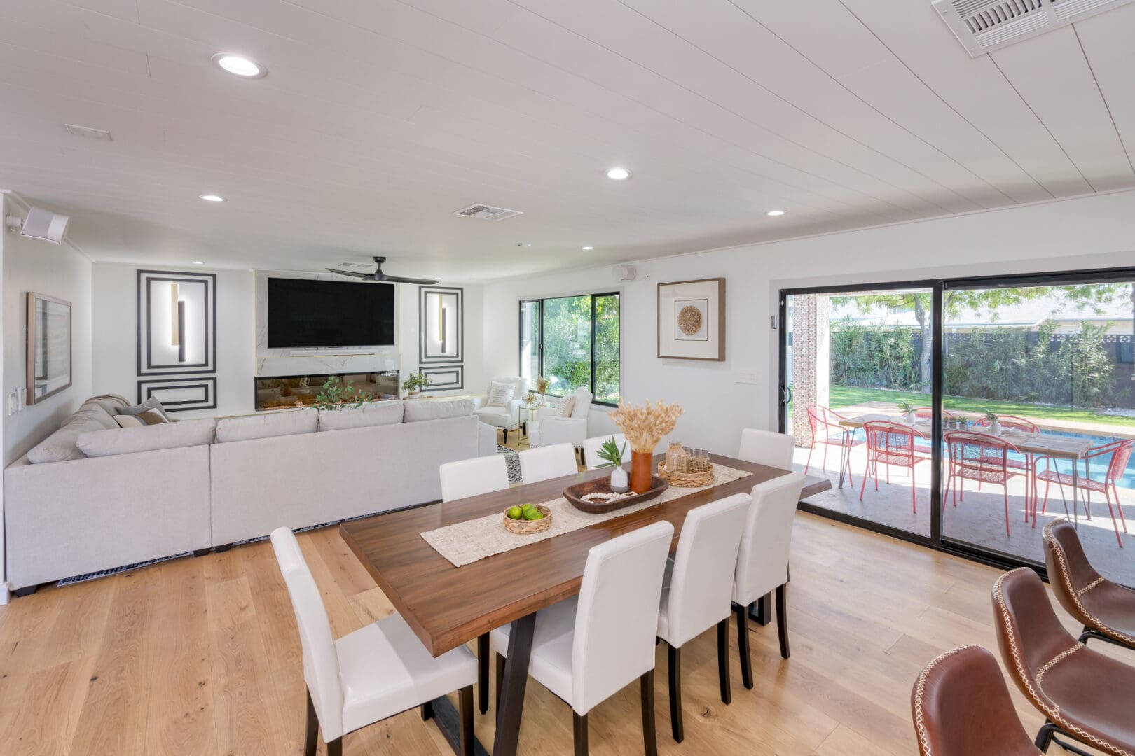 A dining room table with white chairs and a television.