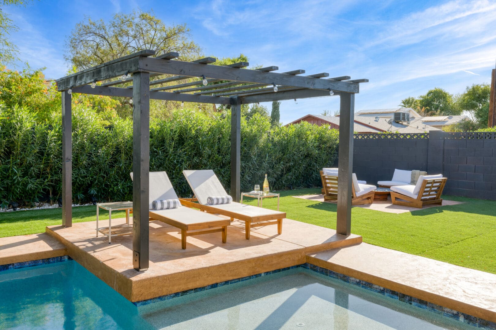 A pool with two lounge chairs and an arbor.