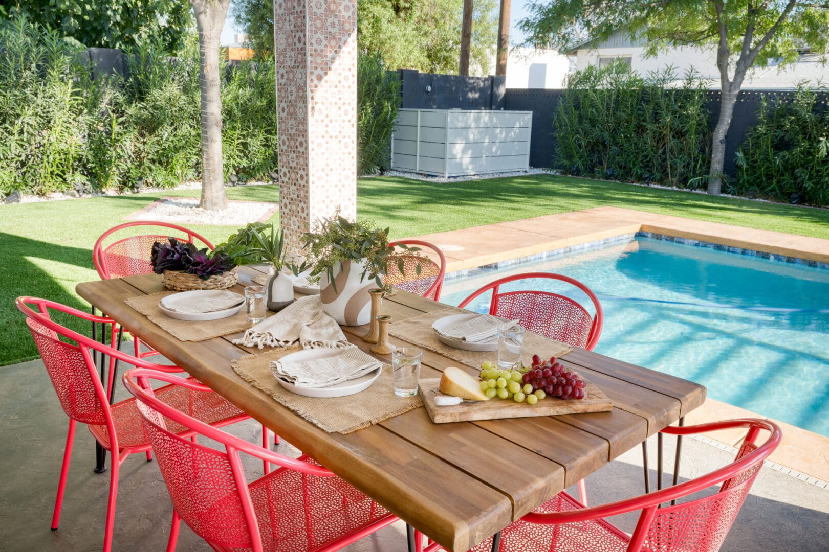 A table with plates and chairs next to the pool.