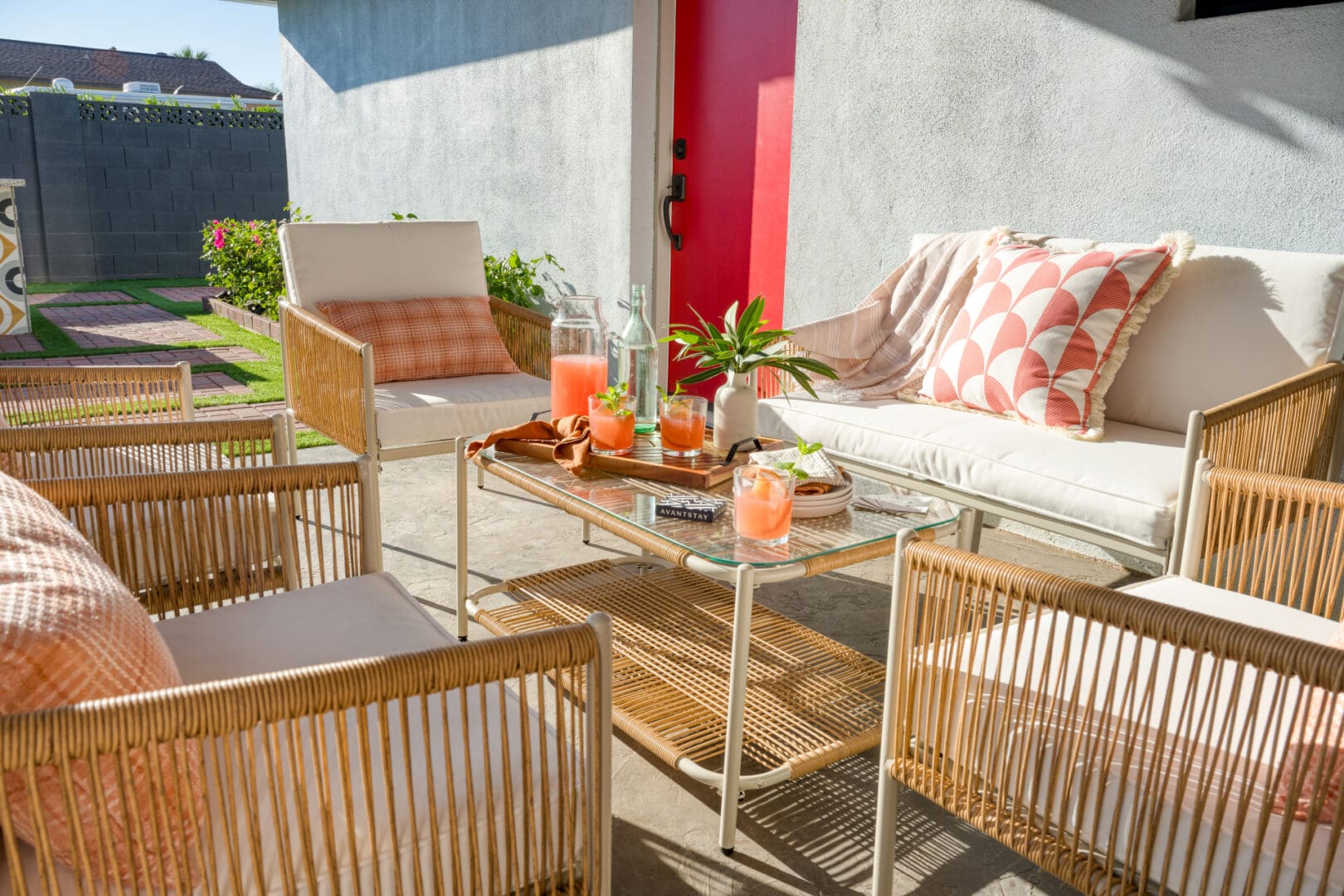 A patio with a table and chairs, pillows, and drinks.