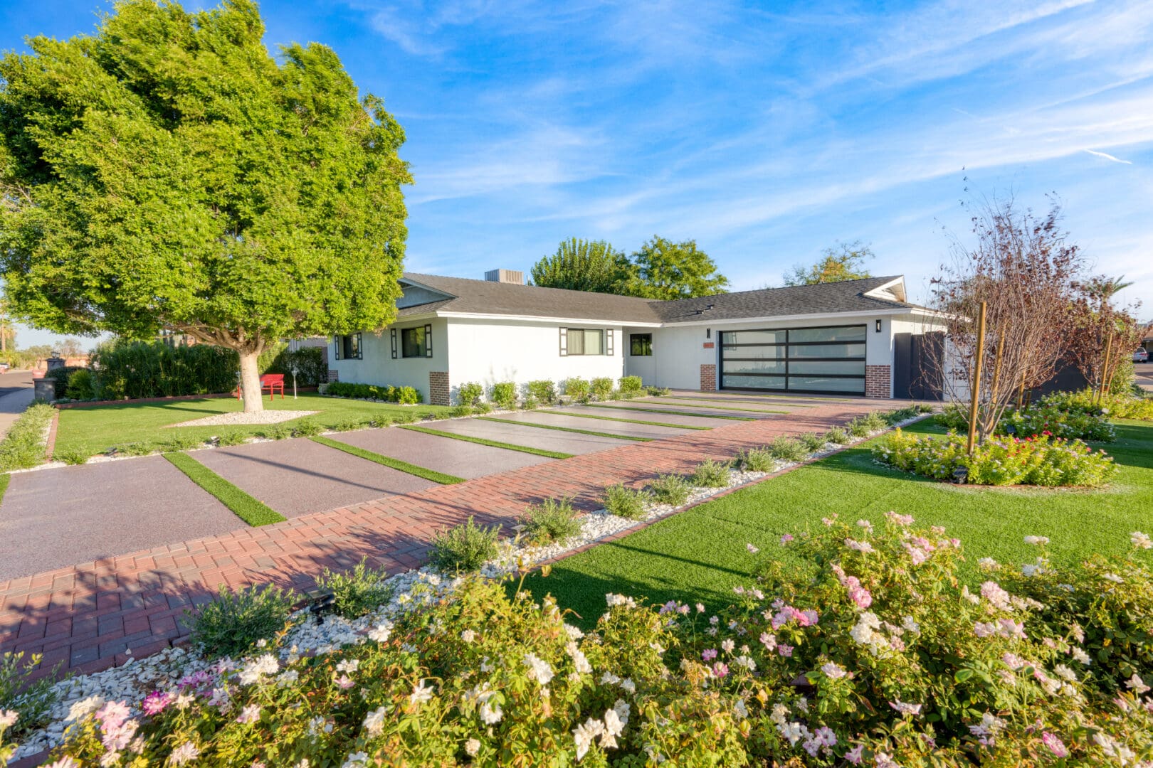 A white house with a driveway and flowers in the yard.