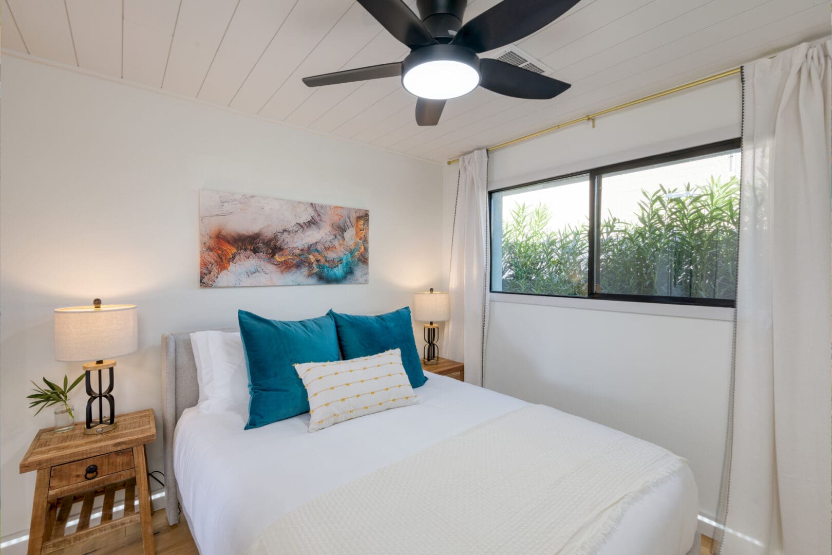 A bedroom with a bed, ceiling fan and window.